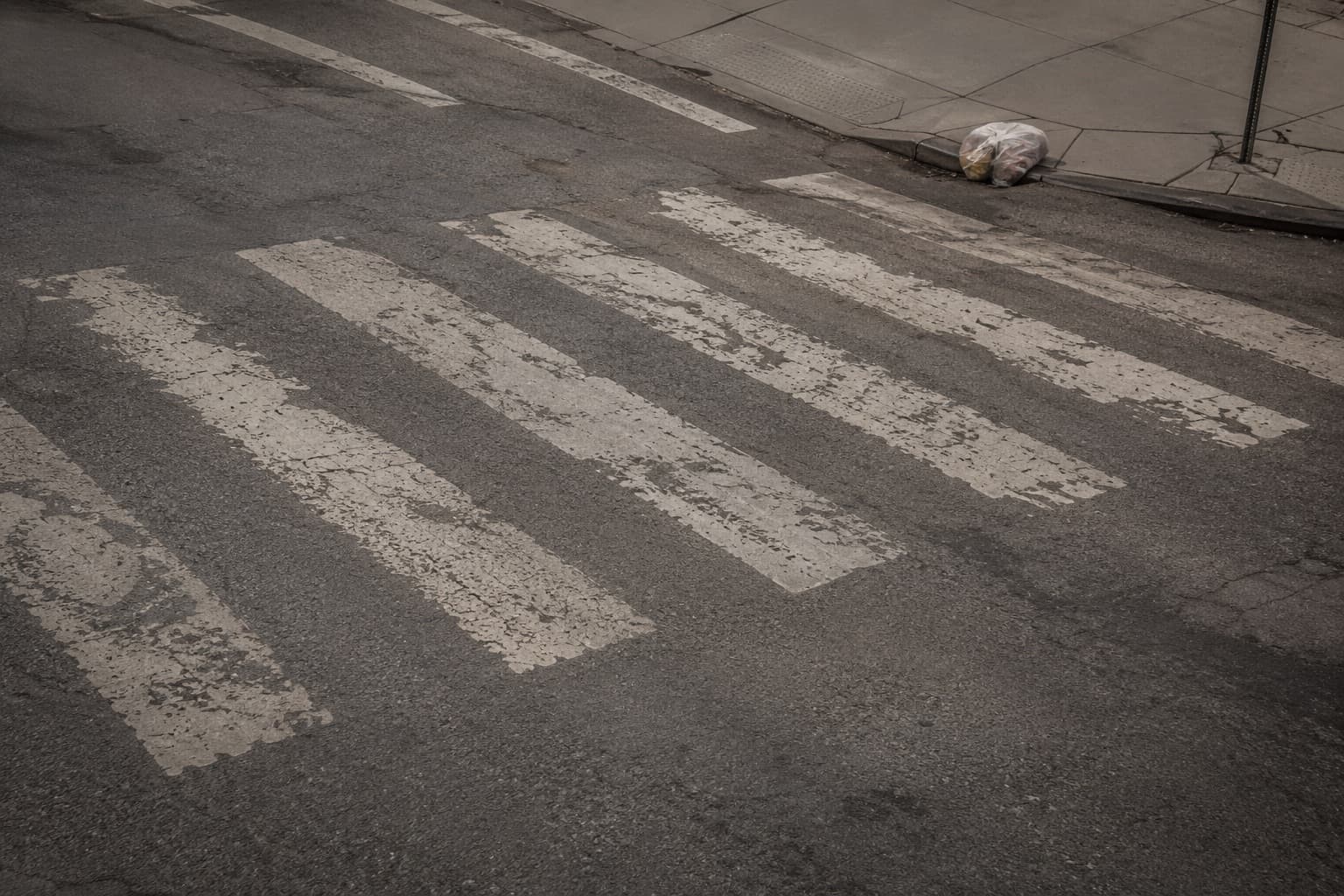 Empty faded crosswalk stripes on worn city asphalt — pedestrian injury claim intake