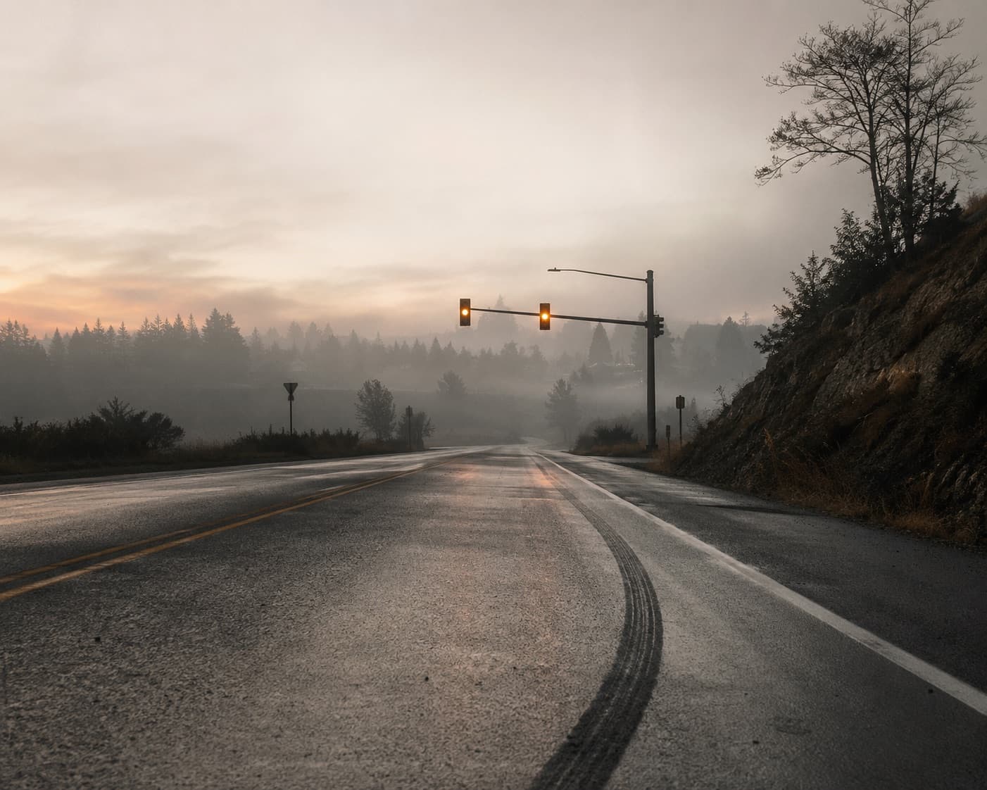 Skid marks curving across a wet two-lane road at dawn, mist rising off the asphalt