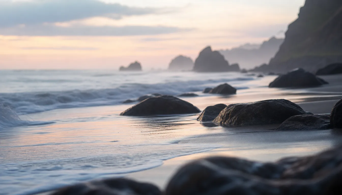 Waves washing over dark rocks on a misty shoreline at dawn, sea stacks fading into the distance — the recurring tide of mass-tort cycles.